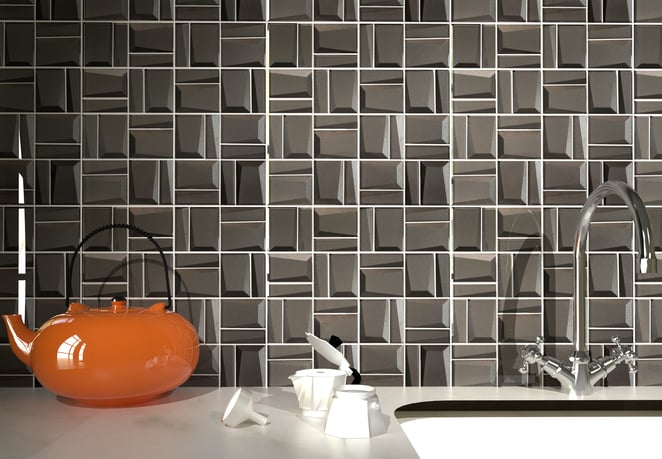 Grey geometric tiles with a glossy finish on a wall, featuring an orange teapot and a silver faucet.