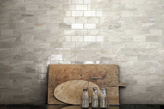 Light gray stone tile wall with a wooden cutting board and glass bottles in front.
